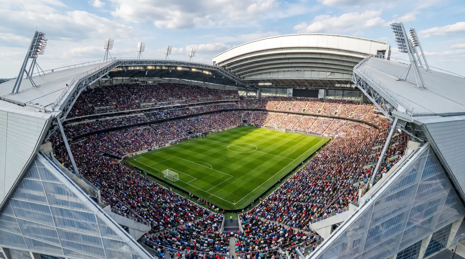 Moderns futbola stadions ar zaļu laukumu un pilnām tribīnēm